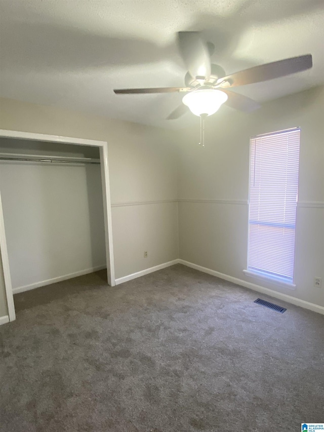 unfurnished bedroom featuring dark colored carpet, ceiling fan, and a closet