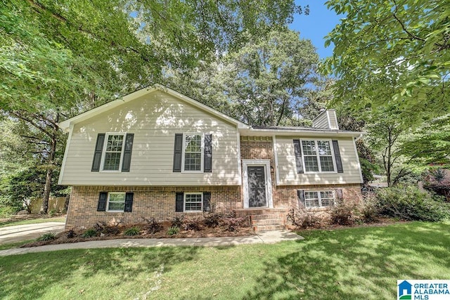 bi-level home with brick siding, a chimney, and a front lawn