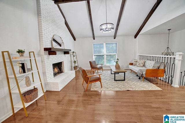 living area with a brick fireplace, beam ceiling, a notable chandelier, and wood finished floors