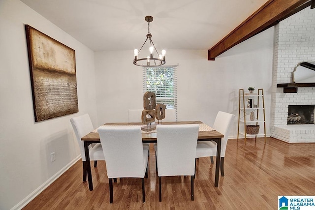 dining area featuring beamed ceiling, a fireplace, wood finished floors, and baseboards