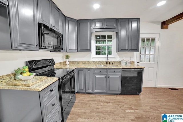 kitchen featuring light stone counters, gray cabinetry, a sink, black appliances, and light wood finished floors