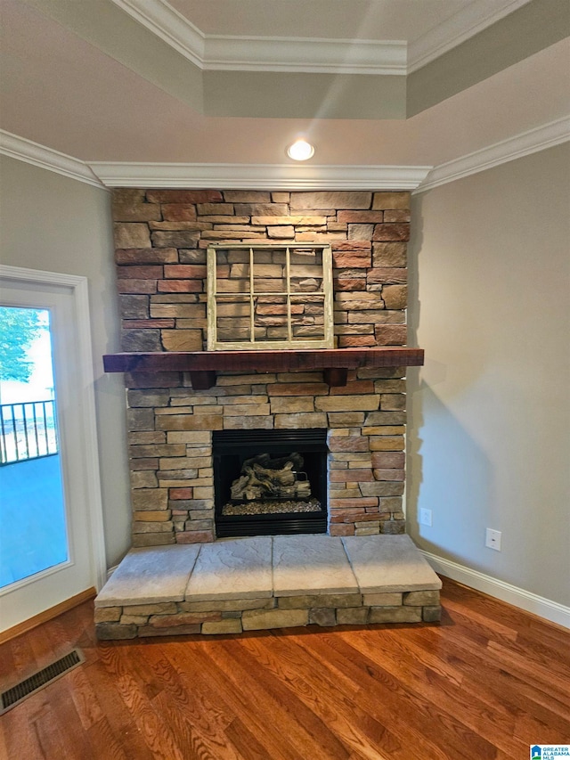 details with a stone fireplace, crown molding, a raised ceiling, and hardwood / wood-style floors