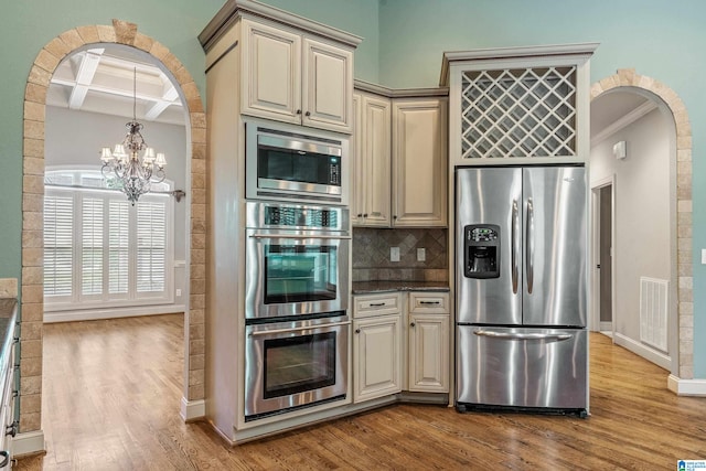 kitchen with cream cabinets, appliances with stainless steel finishes, light wood-type flooring, crown molding, and coffered ceiling