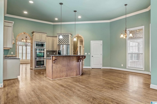 kitchen featuring appliances with stainless steel finishes, hanging light fixtures, light wood-type flooring, and a kitchen island