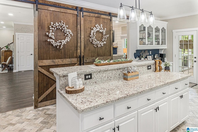 kitchen with a barn door, white cabinets, glass insert cabinets, hanging light fixtures, and crown molding