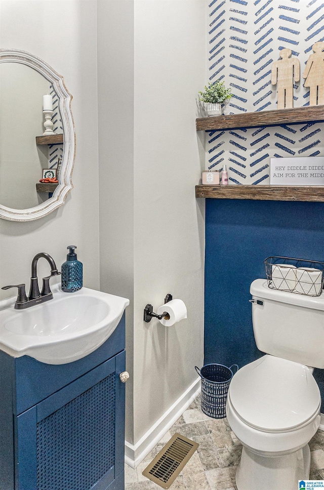 half bath with toilet, vanity, visible vents, and baseboards