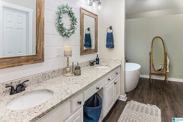 full bathroom featuring double vanity, a freestanding bath, a sink, and wood finished floors