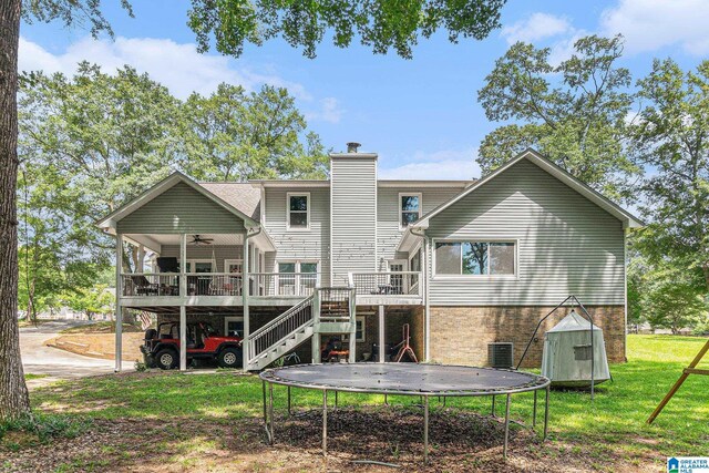 back of property with a deck, a trampoline, a yard, and central AC