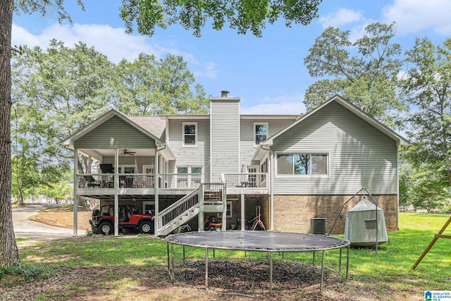 back of house with a deck, stairs, a lawn, a trampoline, and a chimney