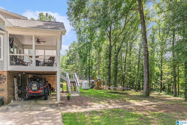 view of yard with driveway, ceiling fan, stairway, a trampoline, and a playground