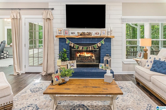 living room with dark wood-type flooring, a brick fireplace, a wealth of natural light, and baseboards