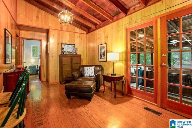 sitting room featuring visible vents, vaulted ceiling with beams, wood walls, and hardwood / wood-style floors