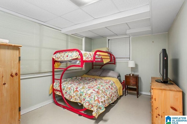 bedroom featuring a drop ceiling, concrete floors, and baseboards