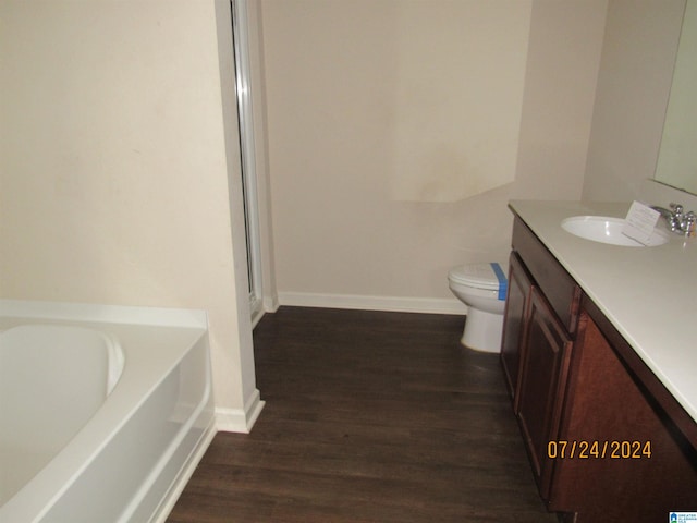 bathroom with toilet, a bath, hardwood / wood-style floors, and vanity