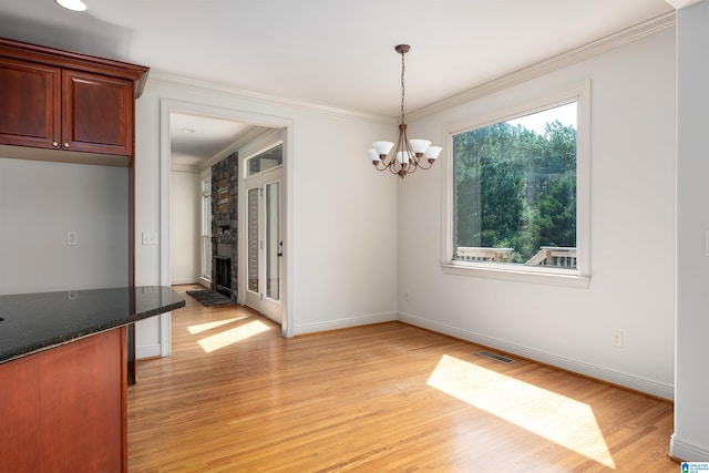 unfurnished dining area with light hardwood / wood-style floors, crown molding, a chandelier, and a large fireplace