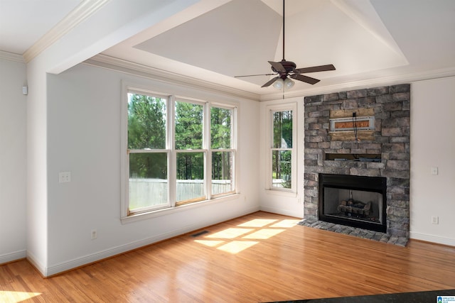 unfurnished living room featuring a stone fireplace, ceiling fan, crown molding, light wood-type flooring, and a tray ceiling