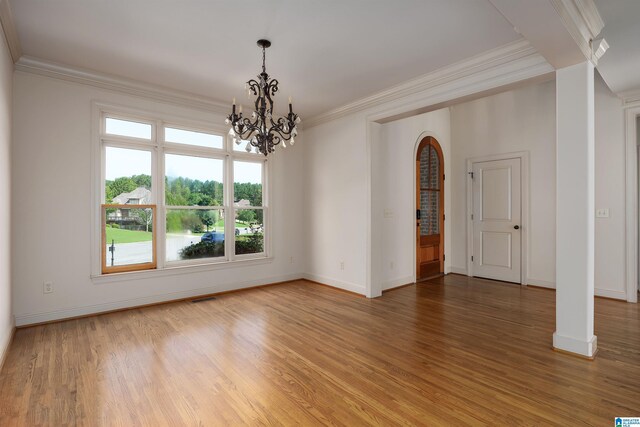 empty room with a notable chandelier, crown molding, and hardwood / wood-style floors