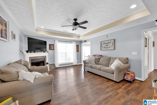 living room with a textured ceiling, a tray ceiling, dark wood-type flooring, and ceiling fan