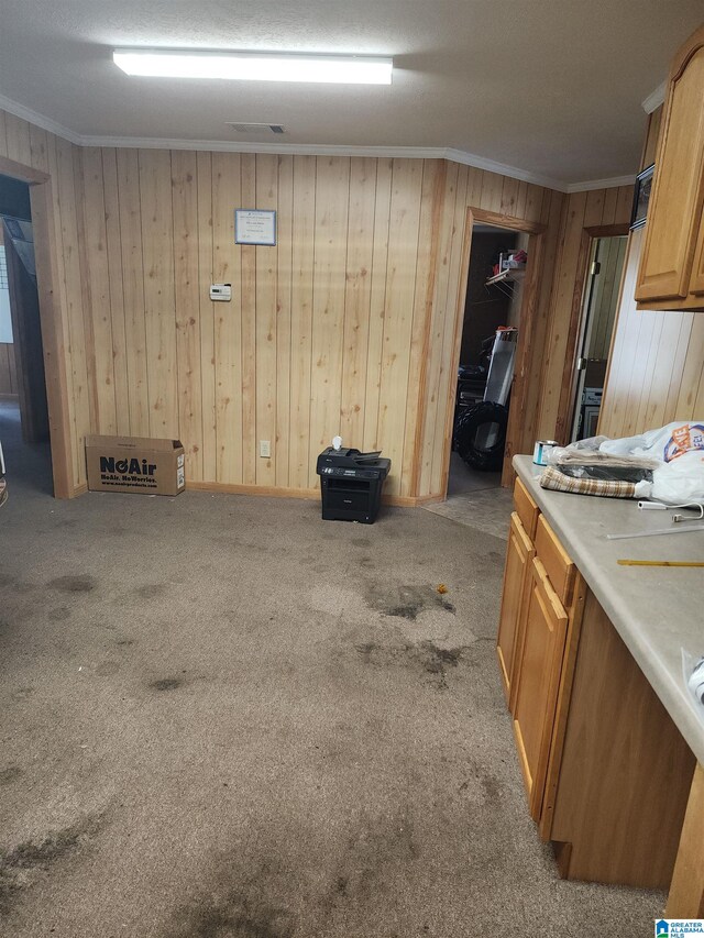 kitchen with wood walls, light colored carpet, and crown molding