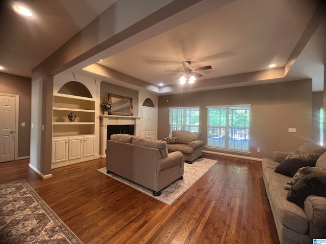 living room featuring dark hardwood / wood-style floors, a tray ceiling, built in features, and ceiling fan