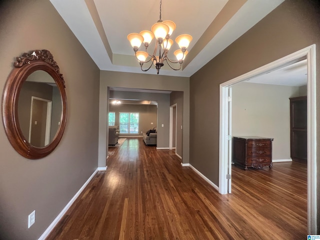 hall with dark hardwood / wood-style flooring, a chandelier, and a tray ceiling