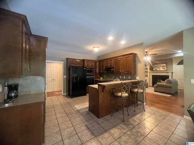 kitchen with a breakfast bar, black appliances, light tile patterned floors, and backsplash