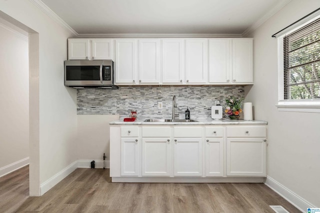 kitchen with stainless steel microwave, a sink, light wood finished floors, light countertops, and backsplash