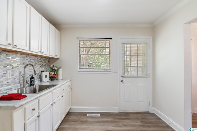 kitchen with a sink, light wood finished floors, tasteful backsplash, light countertops, and white cabinetry