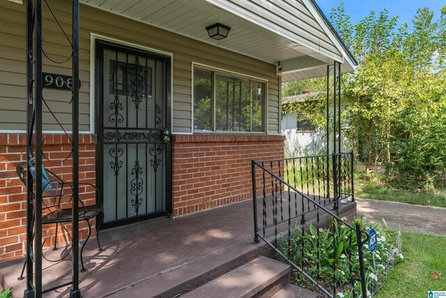 view of exterior entry featuring brick siding and a porch