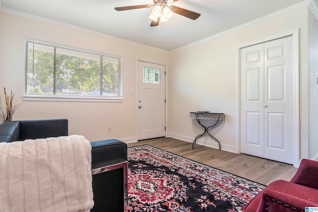 living area featuring wood finished floors, a ceiling fan, ornamental molding, and baseboards