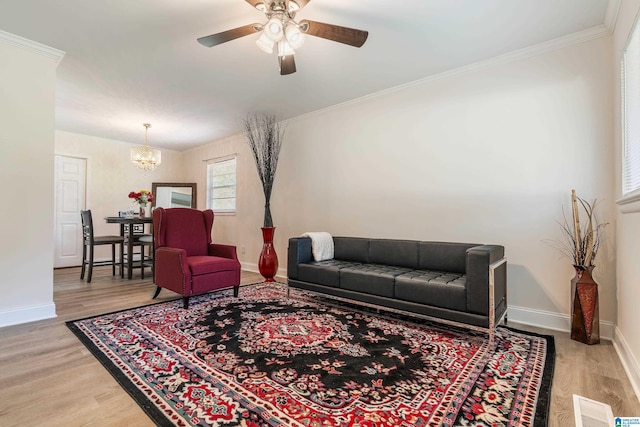 living room featuring light wood-style floors, crown molding, a chandelier, baseboards, and a ceiling fan