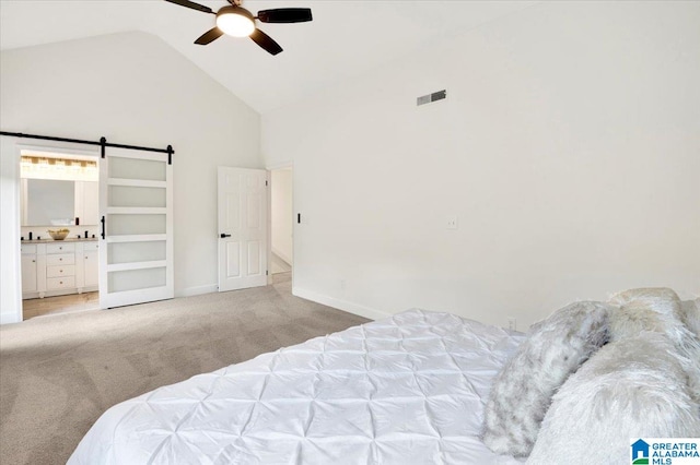 carpeted bedroom with ceiling fan, ensuite bath, a barn door, and high vaulted ceiling