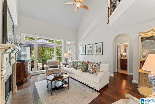 living room with dark wood-type flooring, ceiling fan, high vaulted ceiling, and a high end fireplace