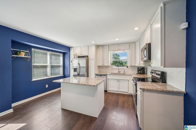 kitchen with sink, a kitchen island, white cabinets, stainless steel appliances, and backsplash