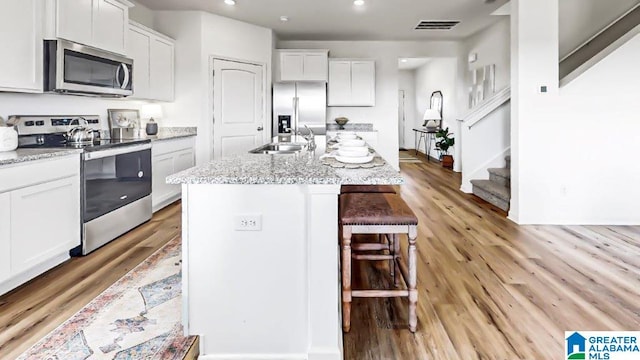 kitchen featuring white cabinetry, a center island with sink, light wood-type flooring, and appliances with stainless steel finishes