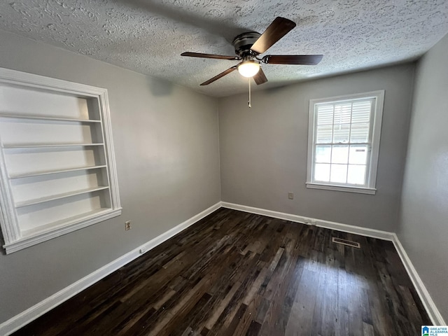 spare room with built in shelves, ceiling fan, dark hardwood / wood-style flooring, and a textured ceiling