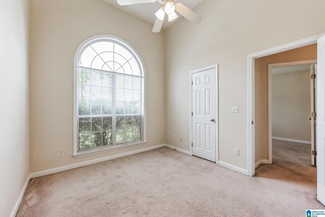 unfurnished bedroom featuring light carpet, multiple windows, high vaulted ceiling, and ceiling fan