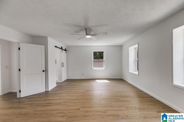 820 Boozer Rd, Heflin, AL 36264 - empty room with a ceiling fan, light wood-type flooring, a barn door, a textured ceiling, and baseboards