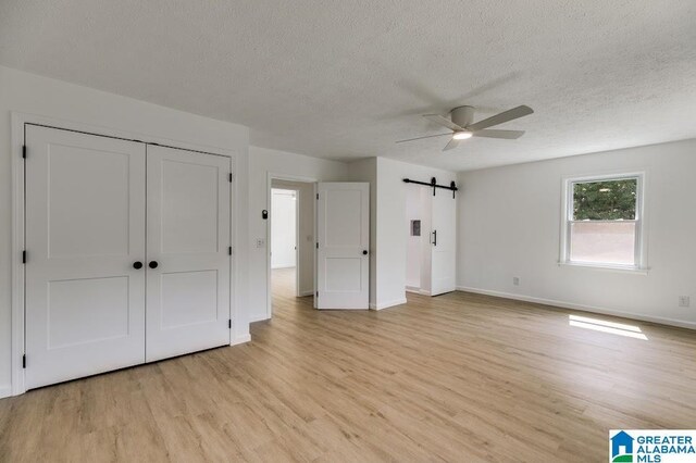 820 Boozer Rd, Heflin, AL 36264 - unfurnished bedroom with light wood finished floors, a barn door, a textured ceiling, baseboards, and a closet