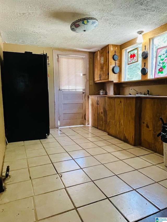 kitchen featuring light tile patterned flooring, black fridge, and a textured ceiling