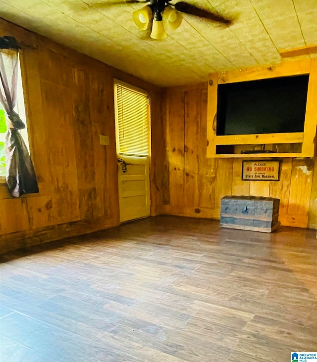 unfurnished living room with hardwood / wood-style flooring, ceiling fan, and wood walls