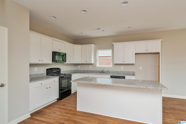 kitchen featuring black appliances, light stone counters, white cabinets, and a center island