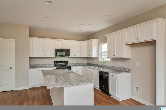 kitchen with light stone counters, a sink, white cabinetry, a center island, and black appliances