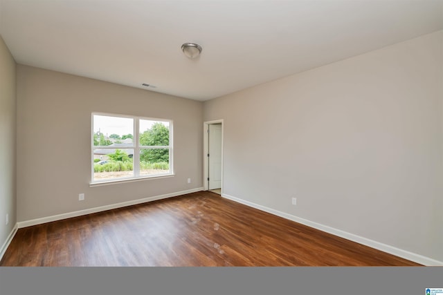 empty room featuring visible vents, baseboards, and dark wood-type flooring