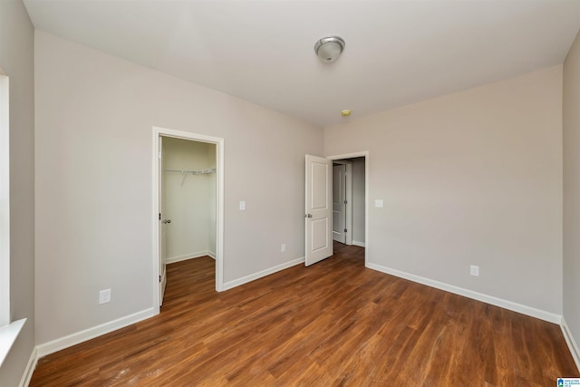 unfurnished bedroom featuring dark wood-type flooring, a walk in closet, a closet, and baseboards