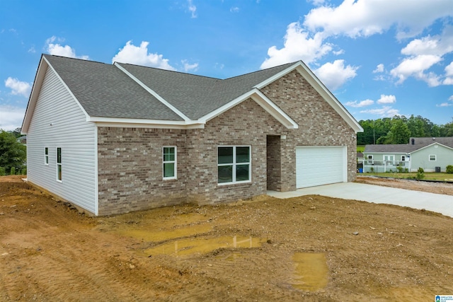 view of front of house with a garage, concrete driveway, brick siding, and roof with shingles