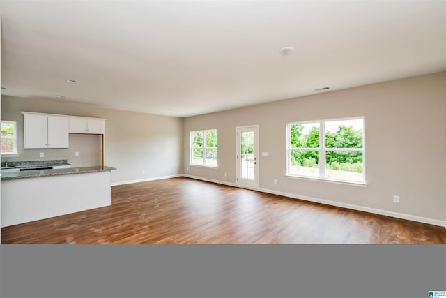 unfurnished living room with dark wood-style flooring, visible vents, and baseboards