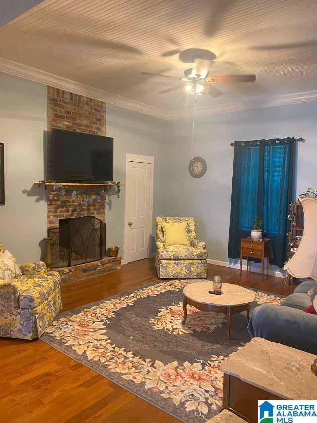 living room featuring ceiling fan, brick wall, hardwood / wood-style flooring, and a brick fireplace