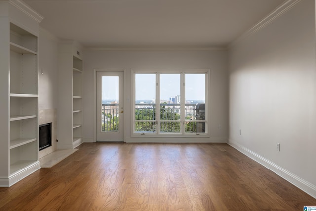 unfurnished living room with hardwood / wood-style flooring, ornamental molding, built in features, and a fireplace