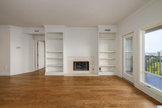 unfurnished living room with hardwood / wood-style flooring, a fireplace, ornamental molding, and built in shelves